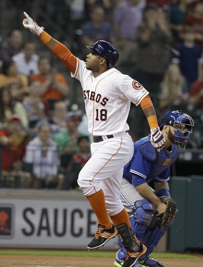 Houston Astros' Luis Valbuena (18) points to the stands as he crosses home plate to score on a solo homerun beside Toronto Blue Jays catcher Russell Martin in the first inning of a baseball game, Sunday, May 17, 2015, in Houston.