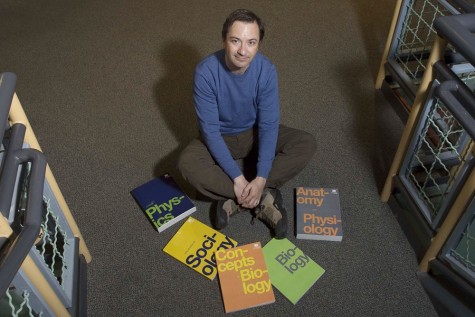 Richard Baranick, Director of OpenStax, sits among five of many college textbooks which are available through the program.